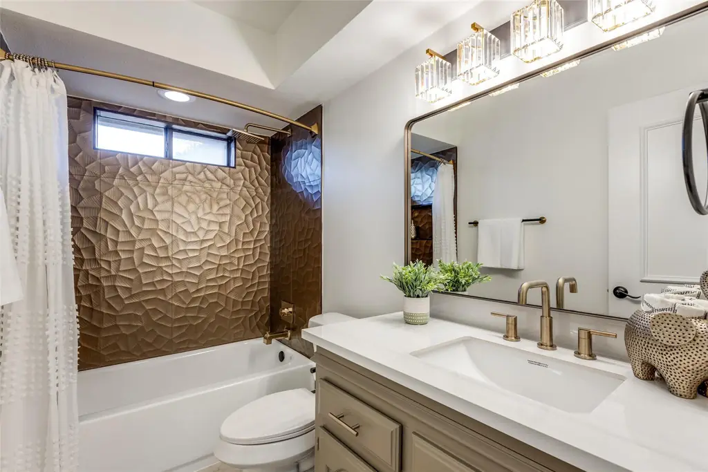 Completed bathroom with a textured tile tub surround, brass fixtures and a quartz vanity top